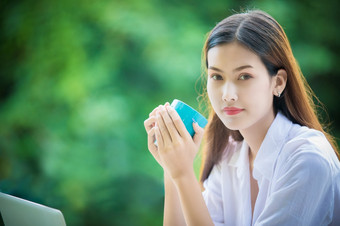 亚洲女人持有咖啡杯为喝和她使用<strong>笔记本电脑</strong>工作<strong>首页</strong>的早....