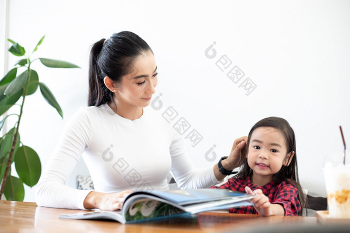 亚洲妈妈。教学她的女儿读书在的学期打破的生活表格和有冷牛奶的表格首页教育概念和活动的家庭
