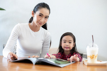 亚洲妈妈。教学她的女儿读书在的学期打破的生活表格和有冷牛奶的表格首页教育概念和活动的家庭