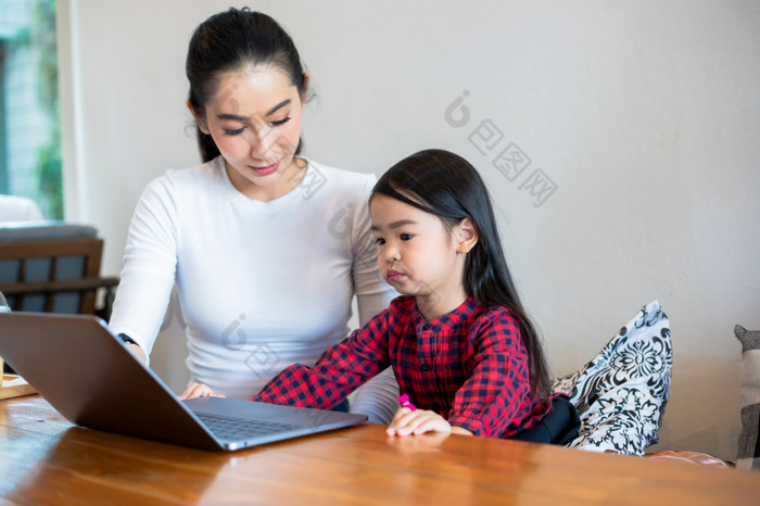 亚洲母亲是教学他们的女儿读书和使用笔记本电脑和技术为在线学习在学校假期首页教育概念和活动的家庭