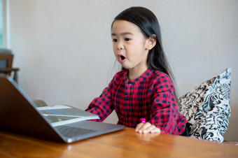 亚洲女孩女儿使用笔记本电脑和技术为在线学习在学校假期和看漫画首页教育概念和活动的家庭