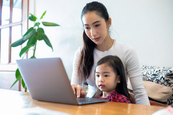 亚洲母亲是教学他们的女儿读书和使用笔记本电脑和技术为在线学习在学校假期首页教育概念和活动的家庭