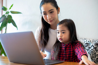 亚洲母亲是教学他们的女儿读书和使用笔记本电脑和技术为在线学习在学校假期首页教育概念和活动的家庭