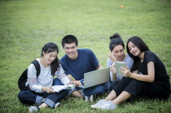 亚洲集团学生使用平板电脑和笔记本分享与的的想法为工作的校园草坪上
