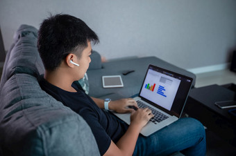 亚洲商人使用无线耳机和使用电脑笔记本工作从首页准备图和信息为在线会议首页
