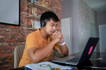 亚洲商人使用<strong>笔记本电脑</strong>和穿耳机为在线会议和工作从<strong>首页</strong>