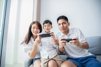 亚洲家庭有有趣的玩电脑控制台游戏在一起父亲和儿子有的手机控制器和的妈妈。欢呼的球员首页
