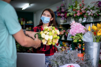 亚洲女人穿脸面具保护面具对冠状病毒危机花店老板小花店业务持有花为交付客户她的商店