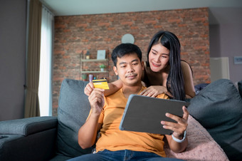 亚洲夫妇购物在线和支付与信贷卡移动PC电脑快乐夫妇首页冲浪的网沙发