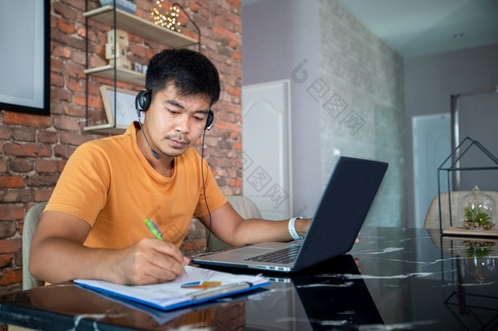 亚洲商人使用笔记本电脑和穿耳机为在线会议和工作从首页