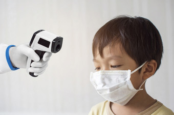 医疗红外温度计手的医生测量的温度的亚洲小男孩病人有穿保护外科手术面具的脸电晕病毒新冠病毒