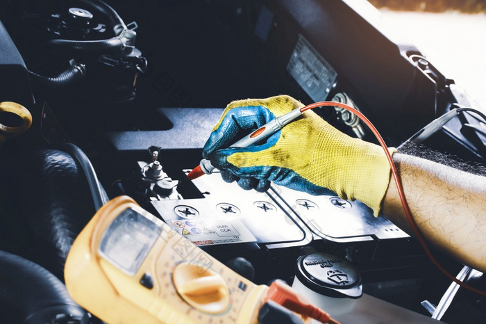 技术员检查电压稳定的的车电池与数字万用表探针