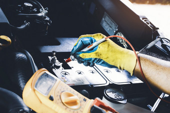 技术员检查电压稳定的的车电池与数字万用表探针
