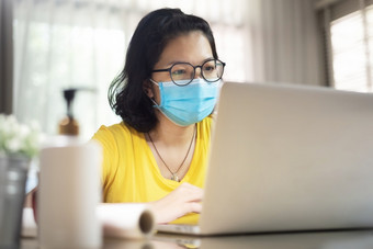 亚洲女设计师穿眼镜使在线视频<strong>会议</strong>与移动PC电脑在检疫和孤立的年轻的女人黄色的衬衫穿<strong>蓝色</strong>的外科手术面具工作从首页在流感大流行病毒科维德冠状病毒健康哪预防保护