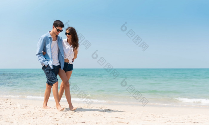 肖像浪漫的年轻的夫妇休闲穿太阳眼镜走的海滩与蓝色的天空快乐微笑英俊的男人。和美丽的女人爱情人约会浪漫
