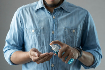 亚洲有胡子的男人。蓝色的衬衫站在灰色背景使用摩擦酒精可移植的喷涂他的手掌和手为防止冠状病毒新冠病毒流感大流行疫情防腐剂卫生和健康的和健康哪概念工作室