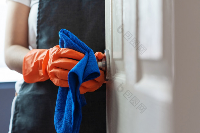 女人手橙色橡胶手套清洁触碰表面通过门把手与蓝色的清洁布消毒为卫生冠状病毒新冠病毒预防概念