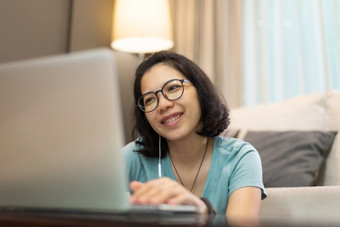 美丽的亚洲女孩蓝色的衬衫和眼镜享受在线类与互联网无线技术快乐微笑年轻的女人使用移动PC电脑在检疫和孤立的工作从首页科维德冠状病毒