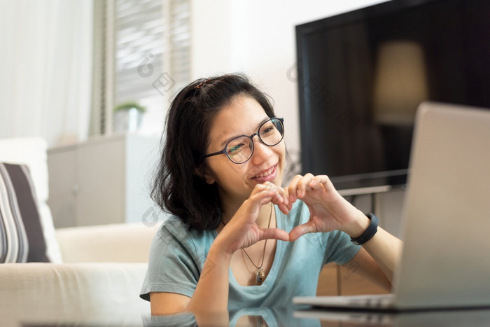 微笑快乐亚洲女人蓝色的衬衫和眼镜使她的手心形状在视频调用与人和她的家庭通过互联网技术移动PC电脑