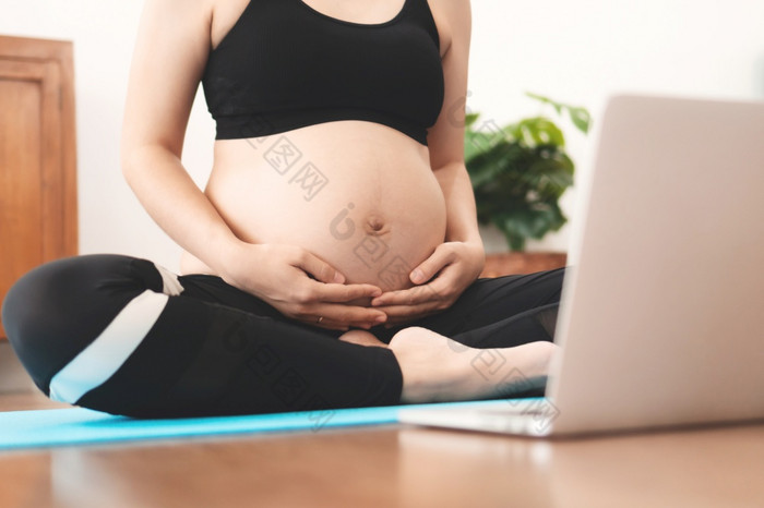 亚洲怀孕了女人练习瑜伽首页与在线视频培训类移动PC女运动服装触碰她的肚子和做练习在怀孕健康的生活方式