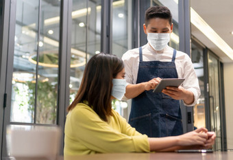 服务员穿保护脸面具采取订单从亚洲女人客户端与数字平板电脑现代咖啡馆餐厅人公共与新正常的生活和生活方式