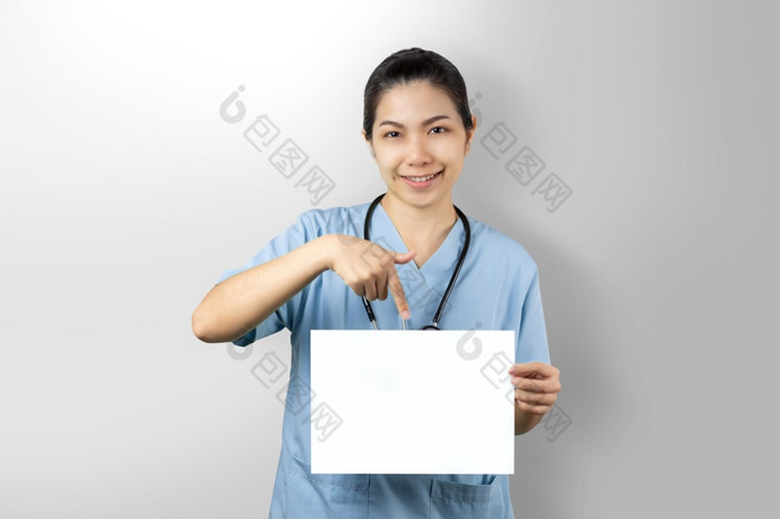 医生女人持有白色模型海报孤立的灰色背景医生指出空白纸表与手指肖像友好的护士穿蓝色的统一的与快乐脸和自信微笑