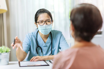 亚洲女人医生蓝色的统一的和保护脸面具给建议高级女病人医院医生穿眼镜和外科手术面具写作信息处方