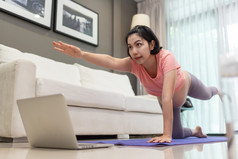 年轻的妈妈。练习瑜伽与在线类移动PC附近沙发亚洲怀孕了女人粉红色的衬衫伸展运动首页准女锻炼首页健康的怀孕和产前哪