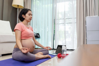 肖像有吸引力的怀孕了女人坐着做瑜伽锻炼莲花位置生活房间健康的年轻的亚洲妈妈。粉红色的<strong>运动服</strong>装与眼睛关闭正念冥想<strong>首页</strong>