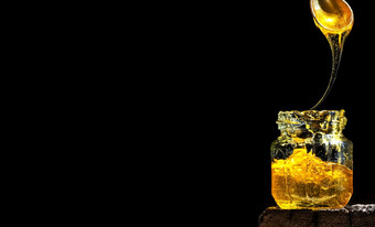 有机自然蜂蜜照亮明亮的阳光玻璃Jar黑色的背景特写镜头复制空间为文本蜂蜜流动从勺子成Jar蜂蜜自然甜点甜蜜