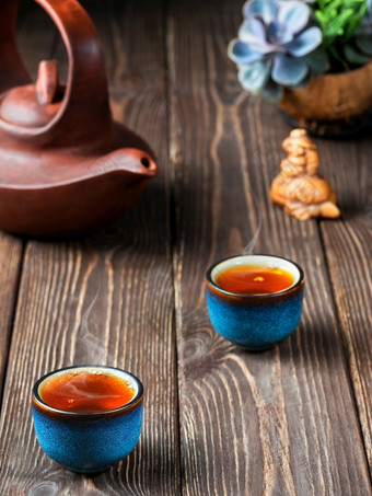 两个碗与红色的茶粘土茶壶的表格茶仪式新鲜酿造黑色的茶蒸汽上升以上的杯温暖的软光黑暗木背景特写镜头