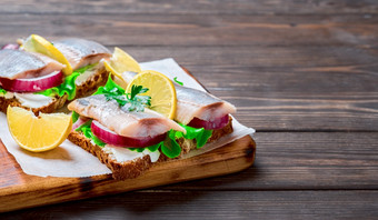 鲱鱼开胃菜快食物概念传统的斯莫雷布罗德三明治鲱鱼三明治与黑麦面包和洋葱装修与欧芹纸表特写镜头木背景与复制空间