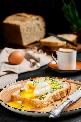 半熟的挖走蛋片面包覆盖与黄油奶油和草本植物粘土板黑色的木表格表示咖啡和面包切片面包模糊背景早餐的想法