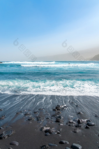 黑色的沙子海滩与岩石海洋波崩溃蓝色的天空和山雾tenerife西班牙黑色的沙子海滩与岩石海洋波崩溃蓝色的天空和山雾tenerife西班牙