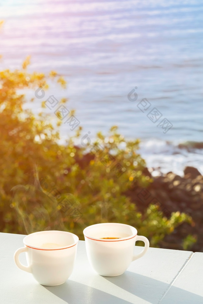 两个杯咖啡阳台与视图的海洋和树的海岸阳光明媚的美丽的早....背景软焦点两个杯咖啡阳台与视图的海洋和树的海岸阳光明媚的美丽的早....背景软焦点