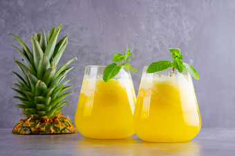 菠萝汁灰色的背景汁为排毒的玻璃菠萝奶昔与新鲜的菠萝健康的夏天喝与薄荷