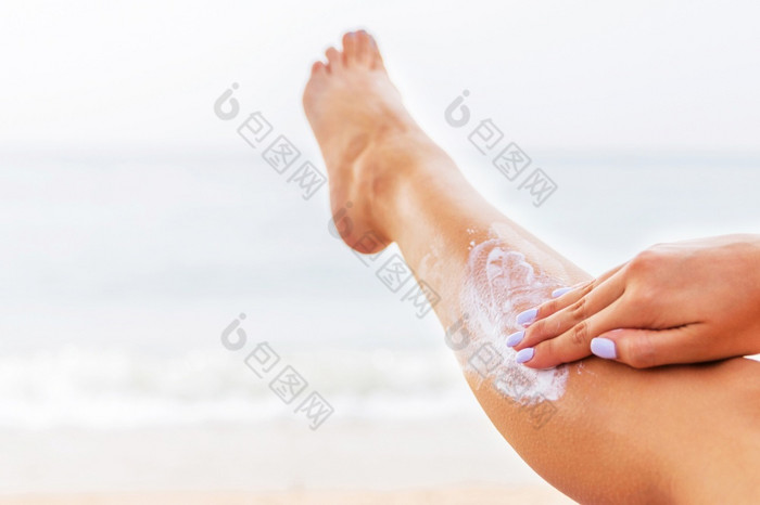 年轻的女人有休息的日光浴浴床的海滩和保护她的皮肤应用防晒霜她的腿年轻的女人有休息的日光浴浴床的海滩和保护她的皮肤应用防晒霜她的腿
