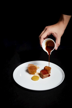 手倒酱汁在食物板精致的菜有创意的餐厅餐概念