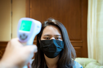 亚洲女人穿面具呼吸保护面具对疫情流感科维德电晕病毒和身体温度健康检查测量发热水平数字红外温度计为医疗保健女人穿面具保护流感与thermoscan