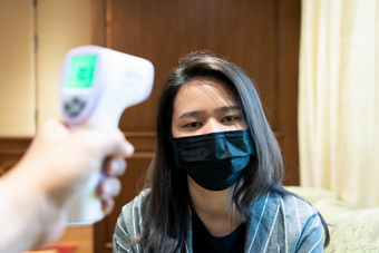 亚洲女人穿面具呼吸保护面具对疫情流感科维德电晕病毒和身体温度健康检查测量发热水平数字红外温度计为医疗保健女人穿面具保护流感与thermoscan