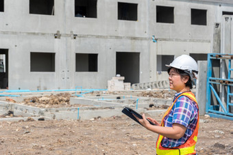 亚洲女人民事建设工程师工人架构师与头盔和安全背心工作和持有无触觉的平板电脑电脑为看到蓝图计划建筑建设网站女人建设工程师建设网站