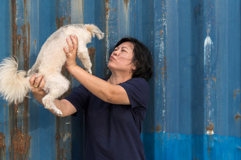 亚洲女人和狗快乐微笑拥抱她的帕特狗可爱的混合品种与shih-tzu波美拉尼亚的和贵宾犬与生锈的蓝色的行业容器背景亚洲女人和狗快乐拥抱与容器