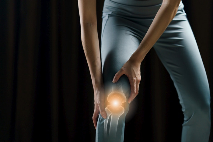 女人持有她的手的膝盖疼痛的膝盖突出显示红色的医学按摩概念