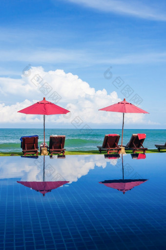 风景热带度假胜地与游泳池附近棕榈海滩阳光明媚的一天日光浴椅子和红色的伞附近的海的海滩开放的公共