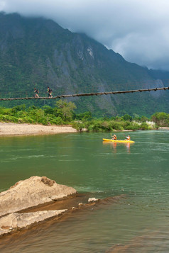 风景的南首歌河的早....欧洲游客皮划艇的河老挝男孩在的悬架人行桥抓住Vieng老挝焦点急流前景