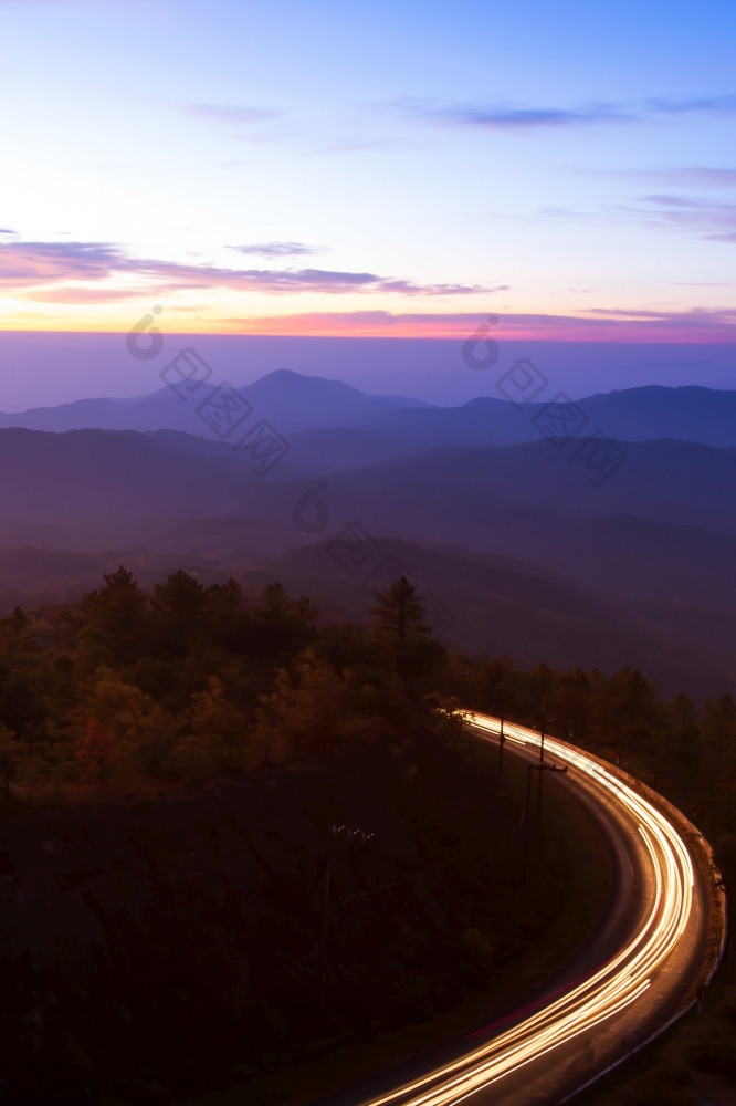 美丽的山路黎明弯曲的山路与光小径对日出天空的背景长曝光