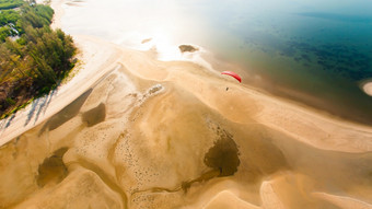 空中视图红色的滑翔伞飞行在岛波浪沙子海滩纹理蓝色的海和绿色红树林森林的背景页泰国焦点滑翔伞