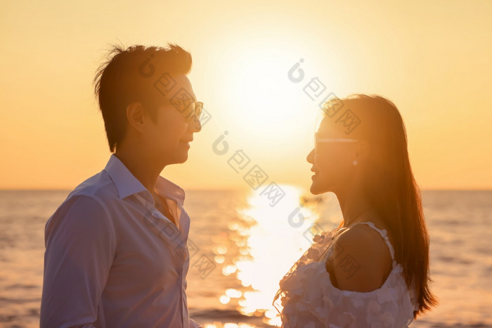 年轻的快乐亚洲夫妇看起来每一个其他的海滩浪漫的旅行度蜜月假期夏天假期亚洲女人和男人。持有手拥抱在户外日落背景