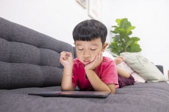 微笑小男孩看起来的触控板说谎舒适的沙发的生活房间享受玩游戏数字平板<strong>电脑</strong>快乐<strong>小孩</strong>子使用有趣的应用程序