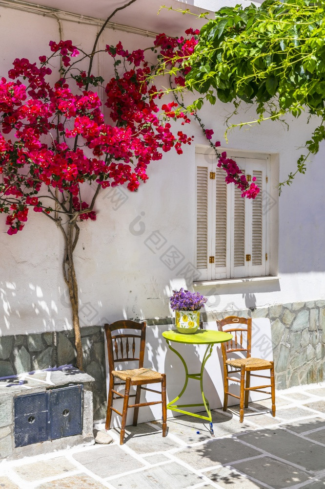 迷人的狭窄的典型的街道希腊岛屿Ios乔拉小镇与粉红色的花树和咖啡表格基克拉迪群岛希腊